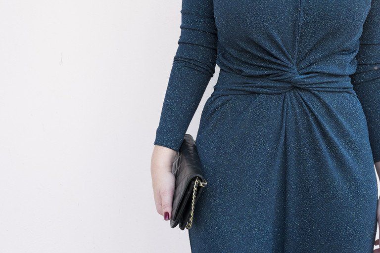 Mulher de vestido azul segurando uma carteira preta contra um fundo branco