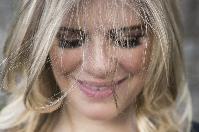 Retrato em close-up de uma mulher loira sorridente com cabelos ondulados e maquiagem suave.