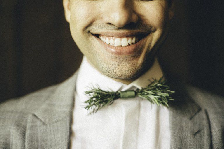 Homem sorridente de terno cinza claro e camisa branca, usando uma gravata borboleta verde.