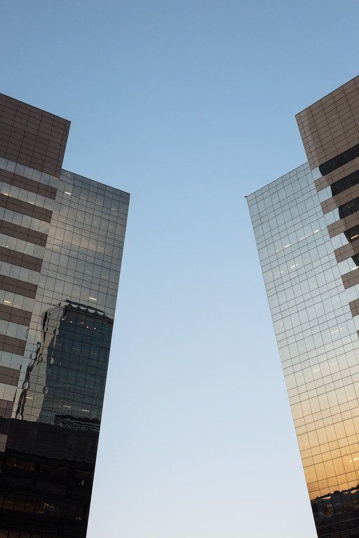 Duas torres de escritórios envidraçadas emoldurando um céu azul límpido ao pôr do sol.