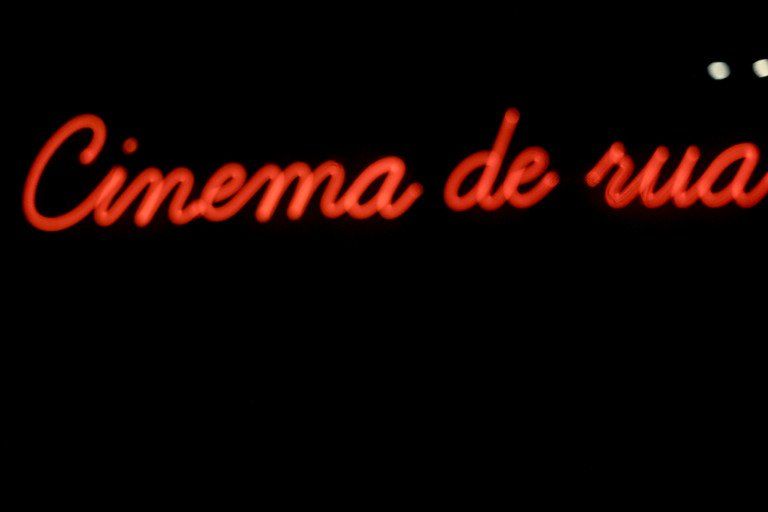 Letras vermelhas em neon com a inscrição “Cinema de rua” sobre fundo preto.