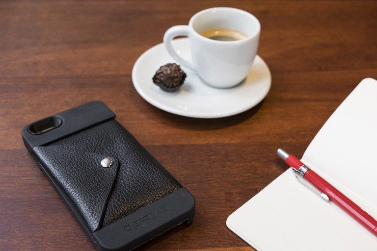 Xícara de café com pires, chocolate, smartphone e caneta vermelha sobre uma mesa de madeira