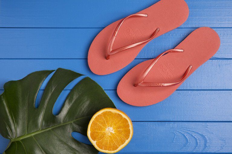 Chinelo coral com fatia de laranja e folha verde sobre uma superfície de madeira azul.