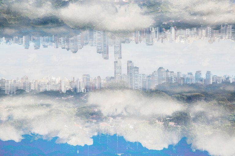 Horizonte da cidade enevoado refletido na água, com prédios altos e nuvens azul-acinzentadas suaves.