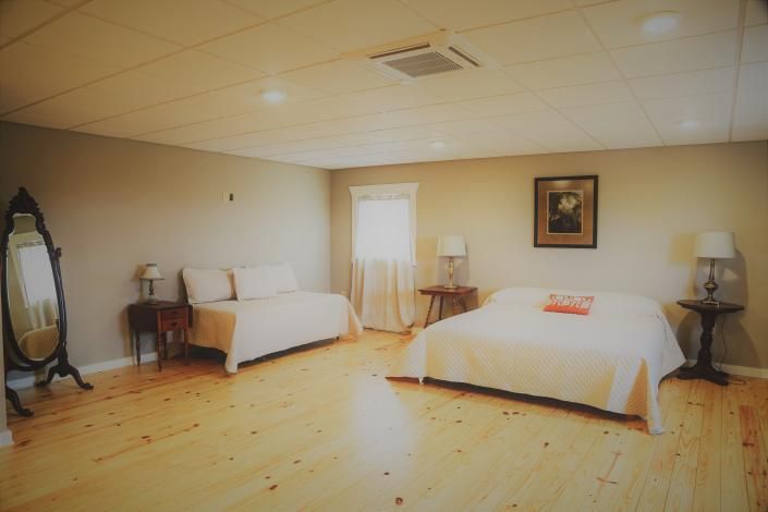 Spacious bedroom with two beds, wooden floor, lamps, and a small desk by a window.