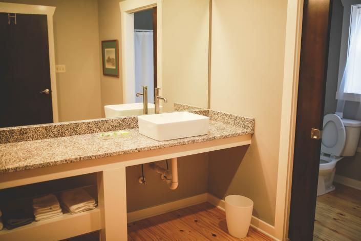 Bathroom vanity with granite countertop, sink, mirror, and toilet visible through an open doorway