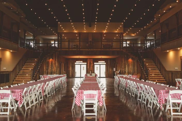 Empty banquet hall with long white-and-red table rows and wooden stairs under warm string lights