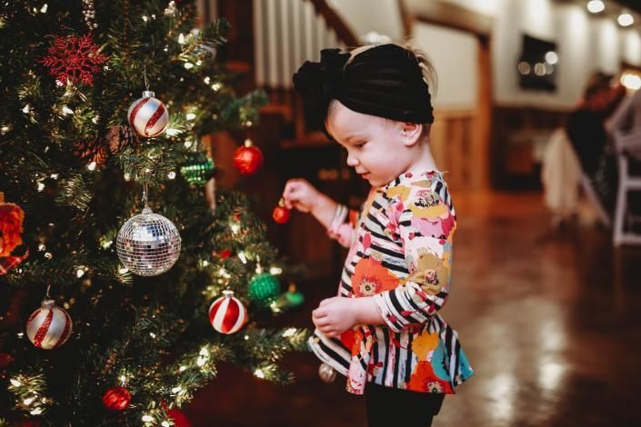 Child decorating a Christmas tree with red and silver ornaments in a warmly lit room