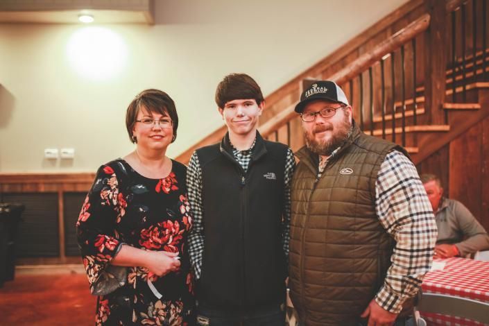 Three people posing indoors at an event, with a staircase and banquet table in the background