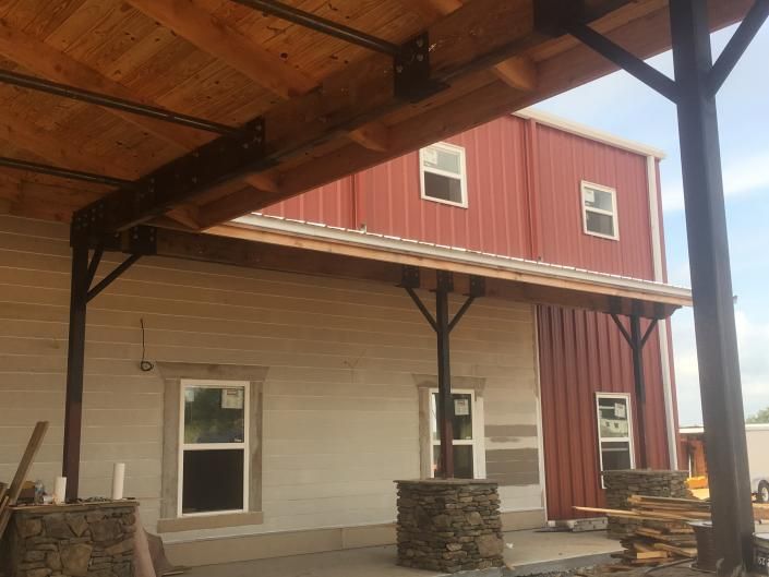 Covered porch attached to a beige and red building with stone columns and wooden beams.