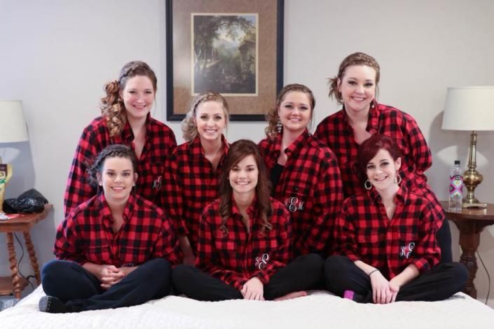 Seven people in matching red plaid shirts posed indoors on a bed, smiling at the camera.
