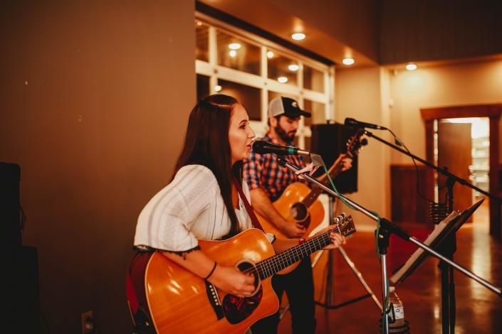 Two musicians performing with acoustic guitars in a warmly lit indoor venue