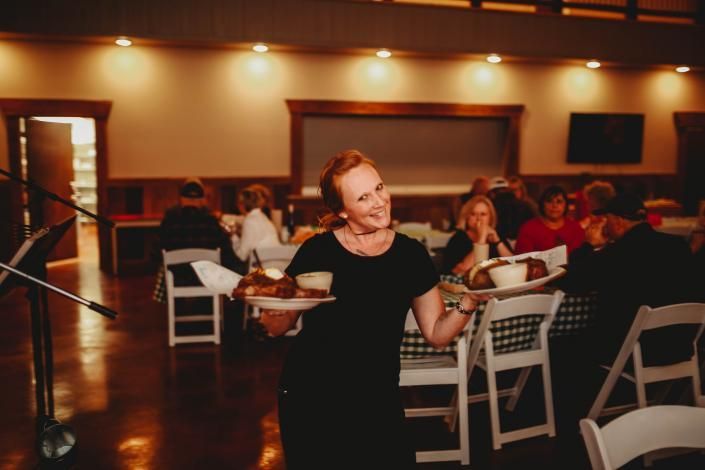 Server carrying trays through a warmly lit restaurant dining room