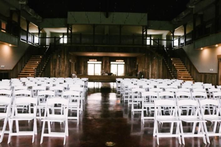 Rows of white folding chairs in a dimly lit indoor hall with a polished floor and stairs on both sides