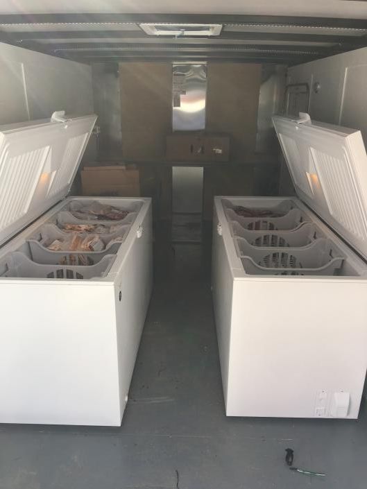 Interior of a refrigerated truck with two open white chest freezers loaded with baskets.