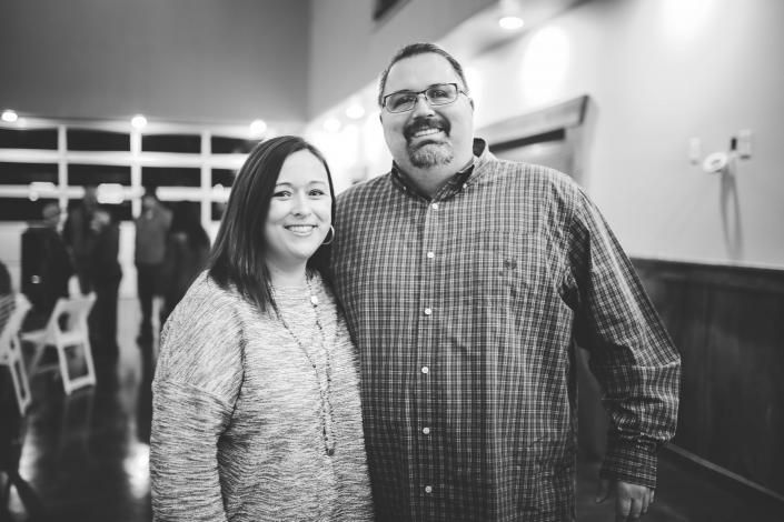 Two people smiling indoors at an event, standing side by side in front of a blurred background.