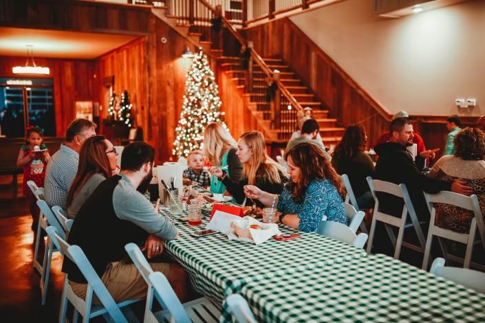 People seated at festive tables in a warm wood-paneled hall with a decorated Christmas tree and staircase
