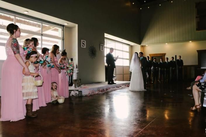 Wedding ceremony in a hall, with bridesmaids in pink and a bride at the altar.