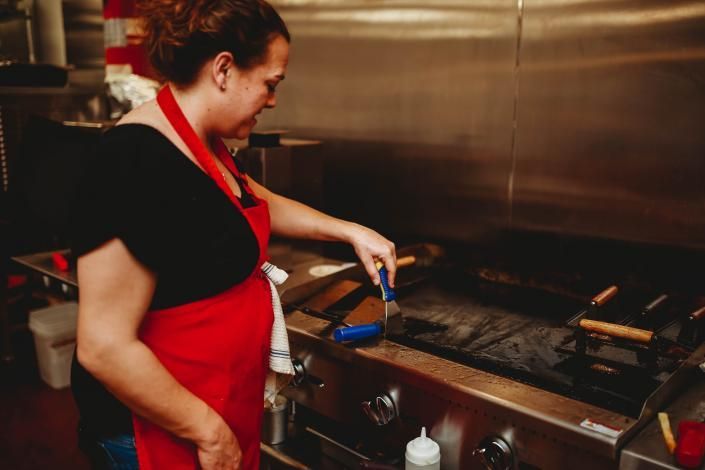 Cook in a red apron working at a commercial stovetop, stirring food with a spatula.