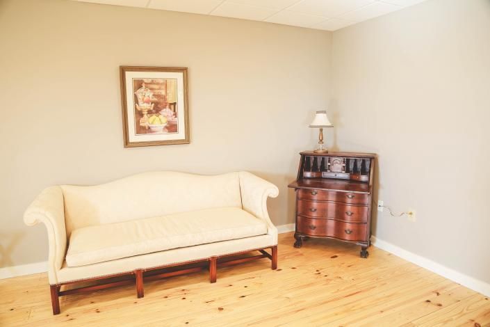 Bright living room with cream sofa, framed wall art, and a small wooden side cabinet with lamp