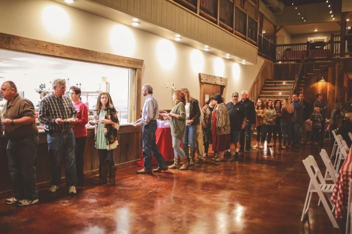 People standing in line along a warmly lit hallway with polished wooden floors at an event venue