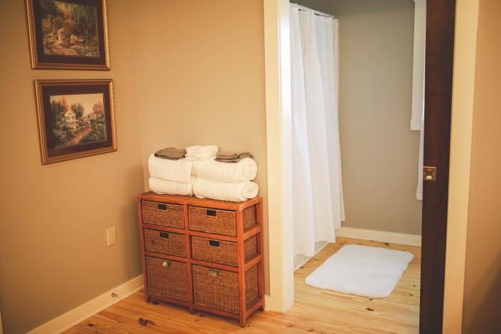 Small bathroom with wicker storage cabinet, folded towels, shower curtain, and white bath mat
