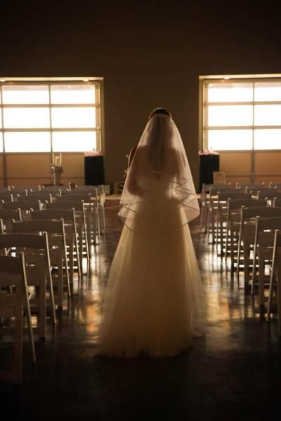 Bride in a white veil and gown walking down an aisle in a softly lit wedding hall