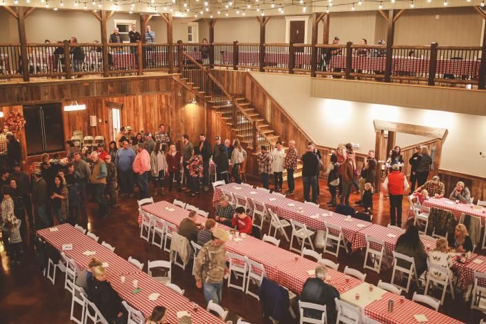 Crowded banquet hall with long tables, seated guests, and a staircase balcony above