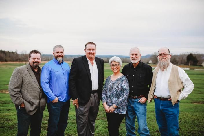 Six people standing together outdoors on a grassy field, smiling at the camera.