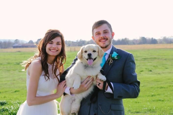 Smiling couple holding a small dog in a grassy field outdoors