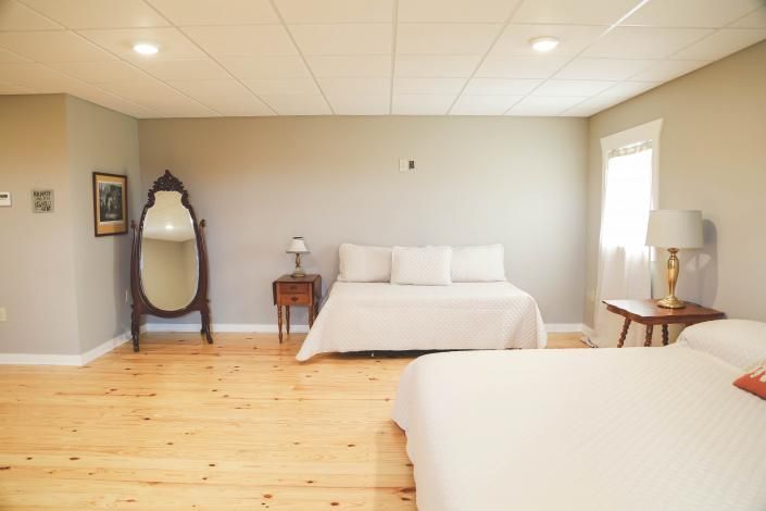 Spacious bedroom with two beds, light wood floors, a mirror, and bedside tables in soft neutral tones