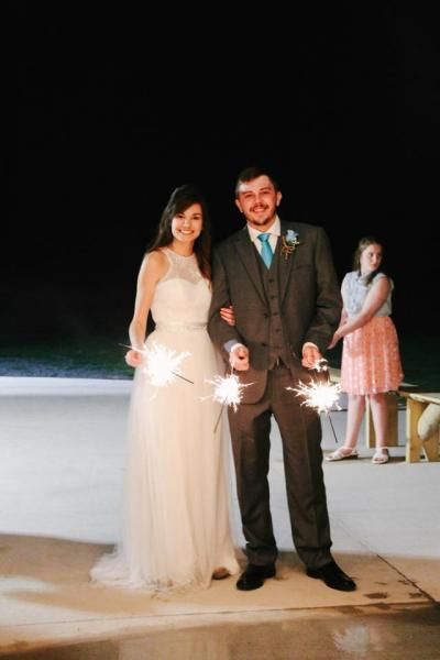 Bride and groom pose at night by a lit fountain, with a child standing behind them.