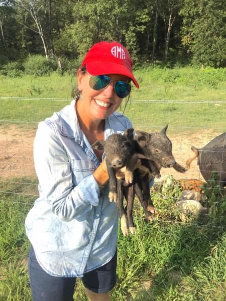 Woman in red cap and sunglasses holding two baby animals outdoors in a grassy field.