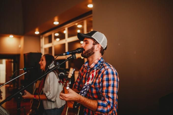 Musician singing and playing guitar on stage with microphone in a warmly lit venue