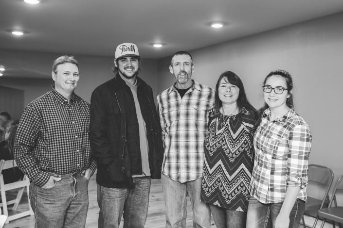 Five people standing together indoors, smiling at the camera in a bright room
