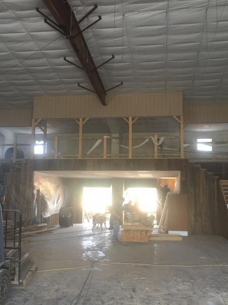 Warehouse interior with bright open doorway, stacked materials, and a lofted wooden structure overhead