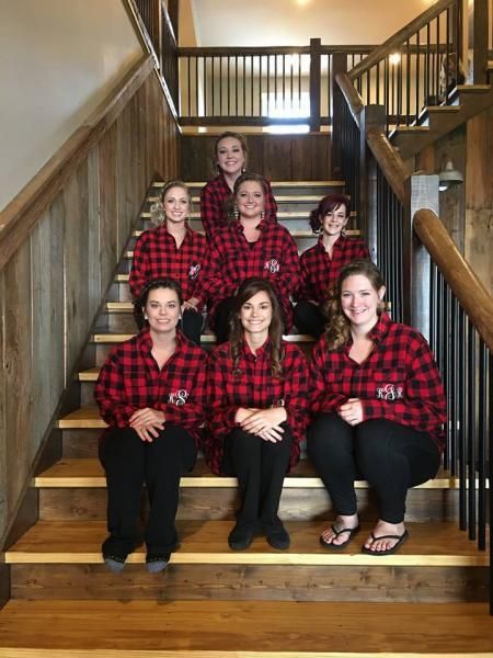 Group of six people in red plaid shirts posing on indoor wooden stairs, smiling at the camera