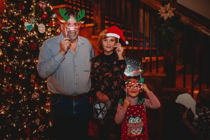 Three people in festive holiday masks pose by a decorated Christmas tree indoors.