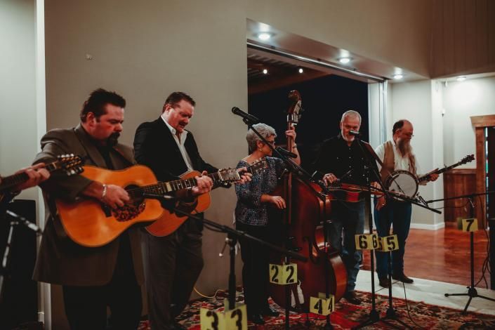 Five musicians playing string instruments on a small stage with microphones in a warmly lit hall