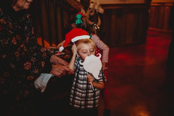 Child in a Santa hat holding a white cutout, with adults nearby in a warm indoor setting