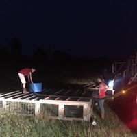 People at night loading a blue bucket onto a low platform in a dark outdoor field