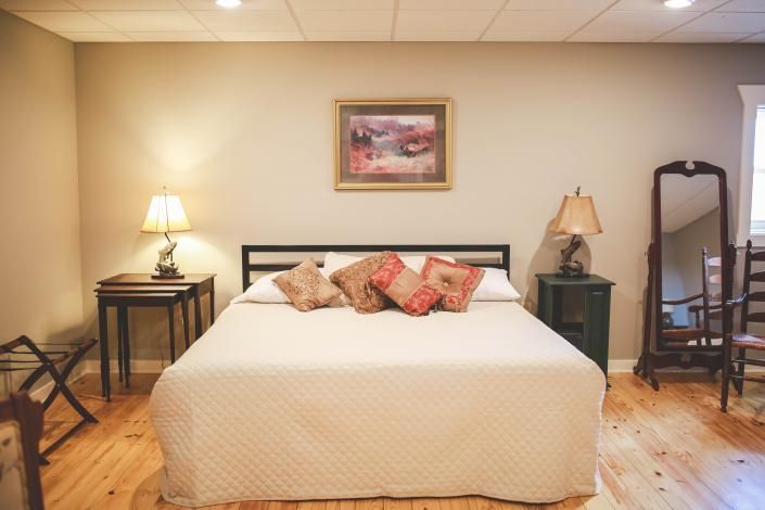Cozy bedroom with a neatly made bed, bedside lamps, wall art, wood floor, and a standing mirror.
