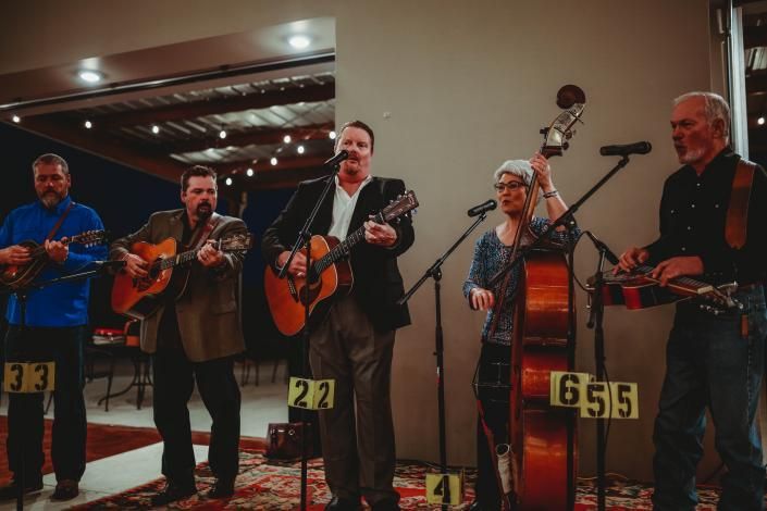 Five musicians perform on stage with guitars and a violin under warm indoor lighting.