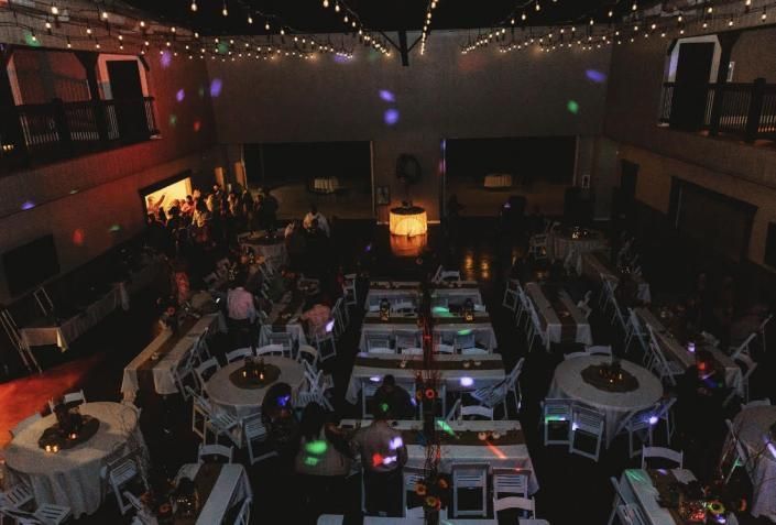 Dimly lit banquet hall with round tables, string lights, and a central glowing centerpiece