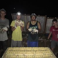 Four people standing behind a table with a woven mat, holding fish at night outdoors