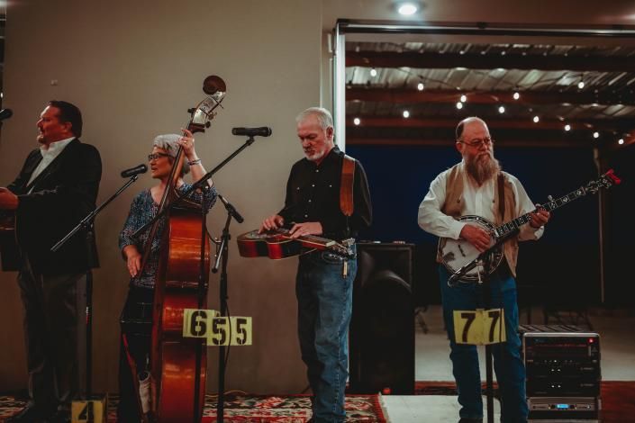 Four musicians perform on a dimly lit stage with microphones and string instruments.