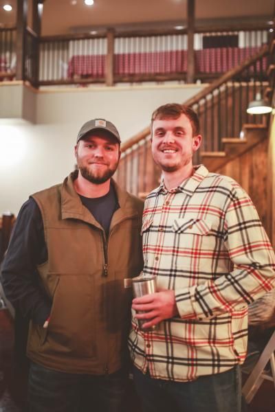 Two men smiling and holding drinks in a warmly lit wooden interior