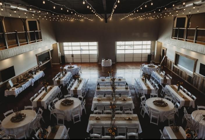 Elegant banquet hall with round tables, white chairs, and string lights under a high vaulted ceiling