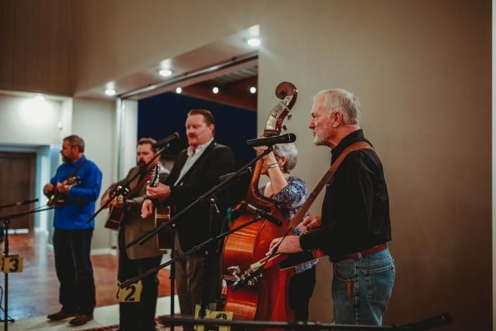 Musicians performing live on stage with guitars and an upright bass, singing into microphones