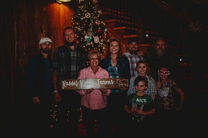 Group posing indoors in front of a lit Christmas tree, holding a holiday sign.